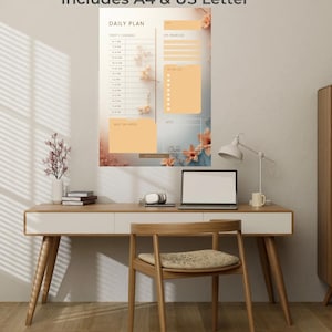 Op de afbeelding: Een afdrukbare dagplanner met de tekst "PRINTABLE DAILY PLANNER Includes A4 & US Letter". De planner bevat secties voor een dagplan, topprioriteiten en een takenlijst. Het ontwerp bevat bloemaccenten.