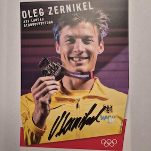 Puede incluir: Fotografía de Oleg Zernikel, saltador de pértiga, sosteniendo una medalla y sonriendo. Lleva una chaqueta amarilla con la bandera alemana y un autógrafo. El texto dice "Oleg Zernikel" y "ASV Landau Stabhochsprung". Los anillos olímpicos son visibles.