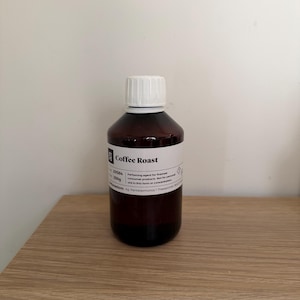 Può includere: Una bottiglia di vetro marrone con tappo bianco, etichettata "Coffee Roast". L'etichetta include testo e un peso di 250g. La bottiglia è su una superficie di legno marrone chiaro contro un muro bianco.