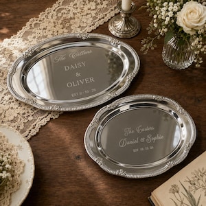 May include: Two oval silver-toned metal trays with ornate embossed edges. The larger tray is engraved with The Cillons, DAISY & OLIVER, and EST 9-16-26. The smaller tray is engraved with The Carters, Daniel & Sophie, and EST 10.15.26.