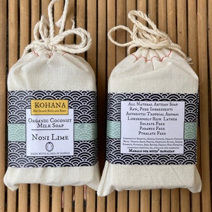 May include: Two bars of handmade soap wrapped in white muslin bags with red stitching. The soap on the left is labeled "KOHANA Big Island Bath and Body Organic Coconut Milk Soap Noni Lime Made with Aloha in Hawaii". The soap on the right is labeled "All Natural Artisan Soap Raw, Pure Ingredients Authentic Tropical Aromas Luxuriously Rich Lather Sulfate Free Paraben Free Phthalate Free Ingredients: Sorbitol, Sodium Cocoate, Organic Coconut Milk, Organic Aloe Vera, Propylene Glycol, Sodium Stearate, Glycerin, Shea Butter, Organic Noni Extract, Lemongrass Essential Oil, Phthalate Free Fragrance Mahalo for Buyin' Hawaiian"