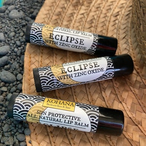 May include: Three black and white lip balm tubes with a sun protection label. The tubes are labeled "Eclipse with Zinc Oxide" and "Kohana Big Island Bath & Body Sun Protective All Natural Lip Balm".