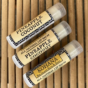 May include: Three lip balm tubes with black and white labels. The top tube says "Pineapple Coconut" and is made with aloha in Hawaii. The middle tube says "Pineapple Coconut" and is an all natural lip balm. The bottom tube says "Kohana" and is an all natural lip balm.