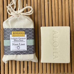 May include: A white bar of soap with the word "ALOHA" embossed on it. The soap is packaged in a white muslin bag with a black and white label that reads "KOHANA Big Island Bath and Body Organic Coconut Milk Soap Noni Lime Made with Aloha in Hawaii".