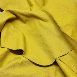 以下が含まれることがあります： 鮮やかな黄色の革のクローズアップ。革は折りたたまれており、質感のある表面です。革の端が見え、素材の厚さと質感がわかります。
