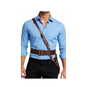 May include: A brown leather shoulder holster with a matching belt. The holster has a strap that goes over the shoulder and connects to the belt. The belt has a large gold-colored buckle and a smaller buckle for the holster.
