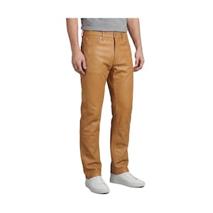 May include: Tan leather trousers with a classic five-pocket design. The trousers have a straight leg cut and a natural, worn appearance. The model is wearing white trainers and a grey t-shirt.