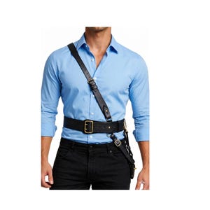 May include: Black leather shoulder holster and belt set. The holster includes a shoulder strap, a belt with a large rectangular buckle, and a smaller strap with a buckle. The leather is a deep black colour.