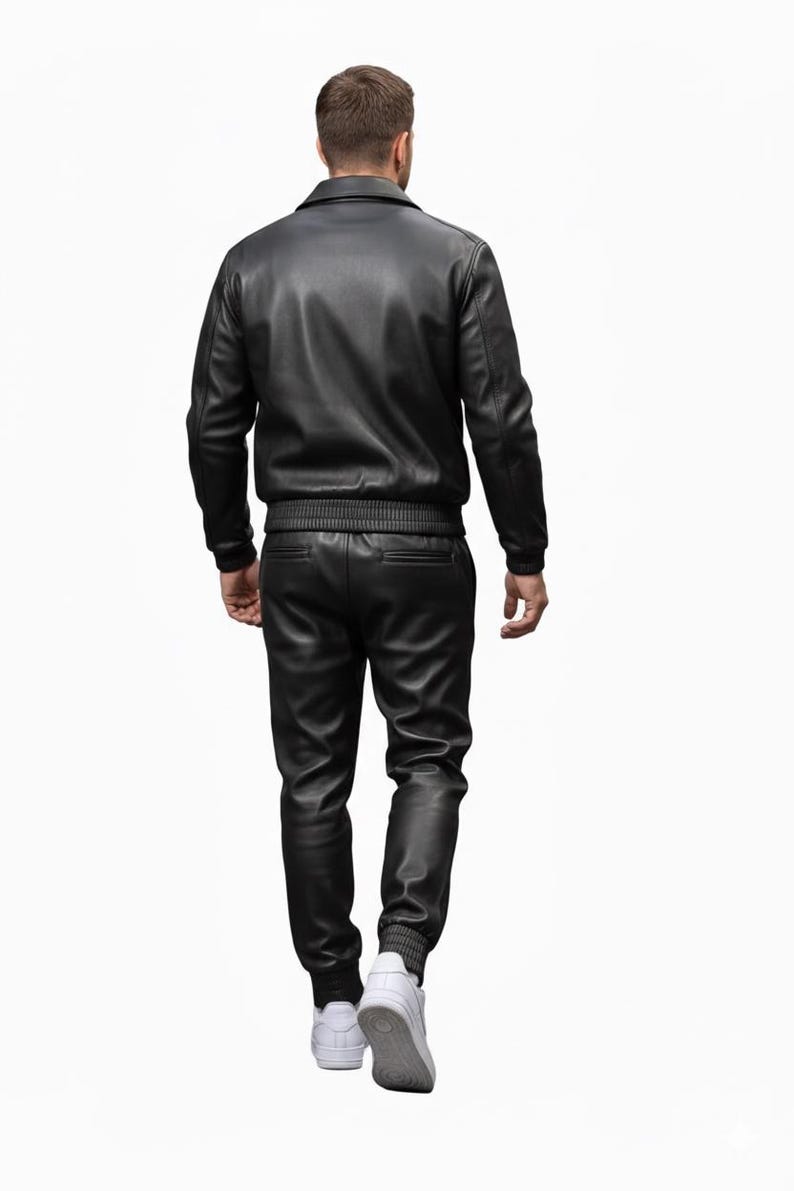 May include: A black leather jacket and matching pants set. The jacket has a collar and ribbed cuffs and waist. The pants have a ribbed ankle cuff. The person is wearing white sneakers.
