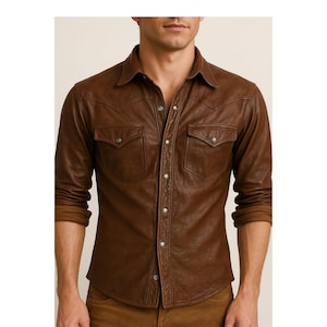 May include: A brown leather shirt with long sleeves, two chest pockets, and a button-down front. The shirt has a classic Western style with a pointed collar and snap closures. The shirt is made of a smooth, supple leather.