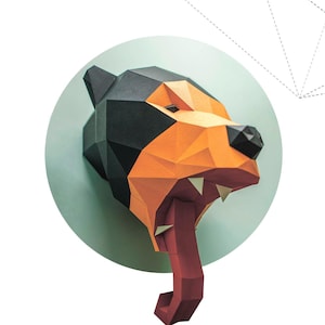 Puede incluir: Escultura geométrica de papel de la cabeza de un oso, con tonos negros, naranjas y rojos. La boca del oso está abierta, mostrando una larga lengua roja. El texto "SUN BEAR" está debajo.