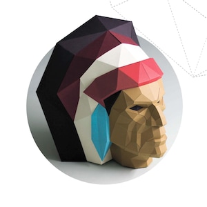 Può includere: Scultura geometrica in carta di un capo nativo americano di profilo. L'acconciatura presenta accenti rossi, bianchi e bordeaux. Un orecchino turchese pende dall'orecchio. Il testo "NATIVE AMERICAN" è sotto l'immagine.