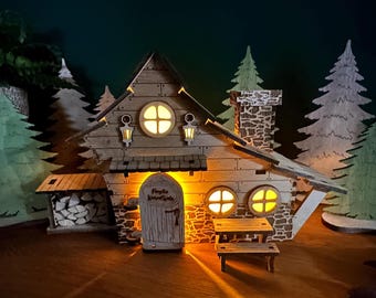 Könnte beinhalten: Ein hölzernes Miniaturhaus mit beleuchtetem Innenraum, ausgestattet mit einem Schornstein in Steinoptik, einer Eingangstür mit der Aufschrift 'Familie Wenzel-Wals', runden Fenstern, zwei Wandlaternen und einem Holzschuppen.