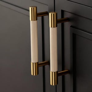 Op de afbeelding: Close-up van zwarte kastdeuren met decoratieve hardware. De kastdeuren hebben een rechthoekig ontwerp. De hardware omvat lange, cilindrische handgrepen met een crèmekleurig midden en goudkleurige uiteinden. De handgrepen zijn horizontaal en verticaal gemonteerd.