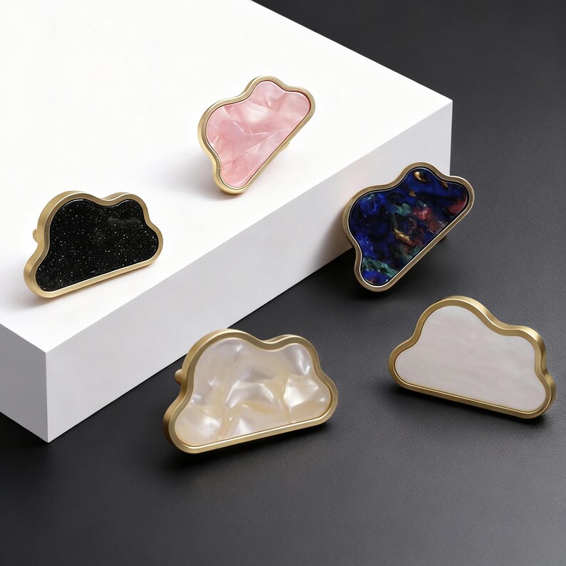 K&ouml;nnte beinhalten: Wolkenf&ouml;rmige Schrankkn&ouml;pfe mit goldfarbenem Rand und verschiedenen Oberfl&auml;chen. Die Kn&ouml;pfe haben schwarze Glitzer-, rosa-, blaue-, wei&szlig;e- und perlmuttartige Oberfl&auml;chen. Diese dekorativen Kn&ouml;pfe sind ideal, um M&ouml;beln eine besondere Note zu verleihen.