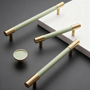 Può includere: Un set di ferramenta per mobili con una combinazione di colori verde chiaro e oro. Il set comprende tre maniglie a barra e un pomello rotondo. Le maniglie a barra hanno un centro cilindrico verde chiaro con estremità e montanti color oro. Il pomello ha un centro verde chiaro abbinato e finiture dorate.