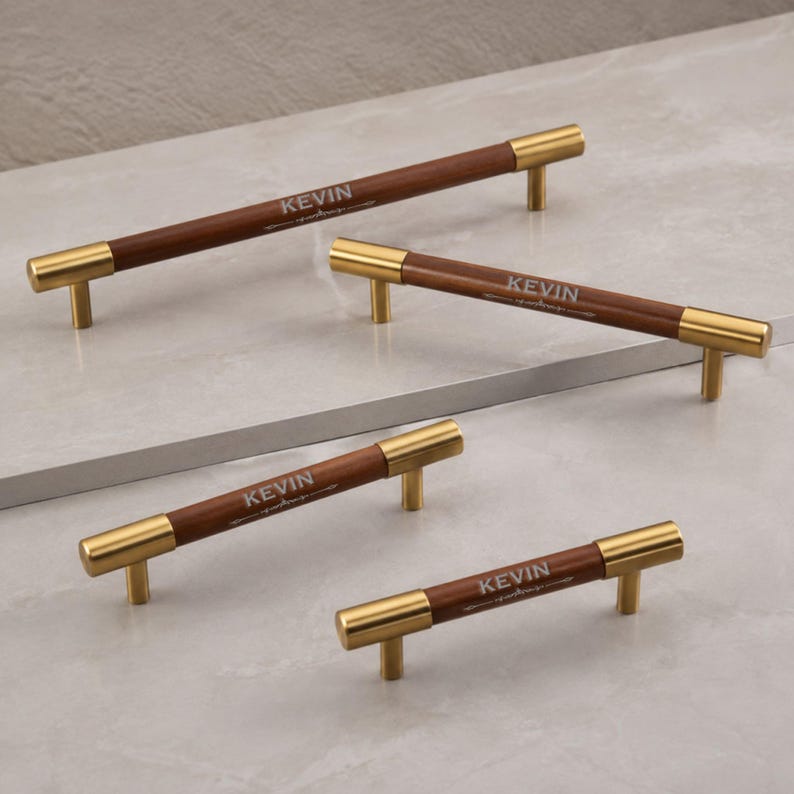 May include: Four cabinet pulls of varying lengths, each featuring a cylindrical dark brown wooden handle with gold-toned metal end caps and mounting posts. The word KEVIN is engraved in a light font on the centre of each wooden handle.
