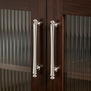 May include: Close-up of a dark brown wooden cabinet with two glass doors. Each door has a long, silver handle. The glass doors have a vertical ribbed texture. The cabinet is likely used for storage.