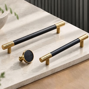 May include: Two long cabinet pulls and one round cabinet knob featuring a black leather-like centre section and brushed gold metal ends. Each piece is engraved with the word CHARLES on the gold metal surface, showcasing a sleek design.