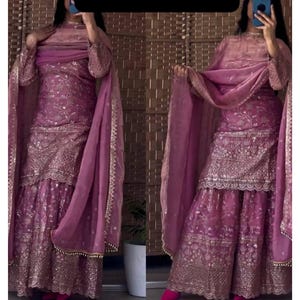Puede incluir: Conjunto magenta de dos piezas con intrincados bordados dorados y un dupatta transparente a juego. El atuendo incluye una parte superior de manga larga y pantalones de pernera ancha. El texto "SanskritiBySatish" se muestra en la parte superior.