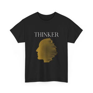 Może przedstawiać: Czarny t-shirt z napisem "THINKER" w białych literach nad złotym, pikselowanym profilem głowy. Projekt jest wyśrodkowany na koszulce.