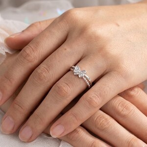 May include: A silver ring featuring a butterfly design with clear gemstones. The ring has a double band with a beaded texture on the lower band. The butterfly is the focal point, with the wings adorned with small, sparkling stones.