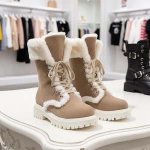 Könnte beinhalten: Ein Paar hellbraune Wildlederstiefel mit weißem Kunstfellbesatz und Schnürsenkeln. Die Stiefel haben eine klobige weiße Sohle und werden auf einer weißen Oberfläche präsentiert.