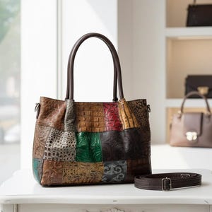 May include: A patchwork leather tote bag with brown handles and a detachable shoulder strap. The bag features a variety of textures and colours, including brown, green, red, and tan. Additional handbags are visible in the background.