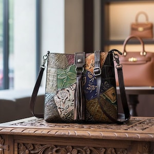 May include: A patchwork leather crossbody bag with a brown leather strap and tassel. The bag features embossed floral and geometric patterns in various colours, including green, blue, and brown. The bag is sitting on a carved wooden table.