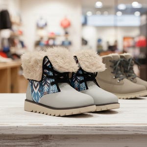 May include: A pair of light gray winter boots with a cream-colored faux fur trim and patterned fabric accents. The boots have a thick, tan sole and black laces. Another pair of boots is visible in the background.