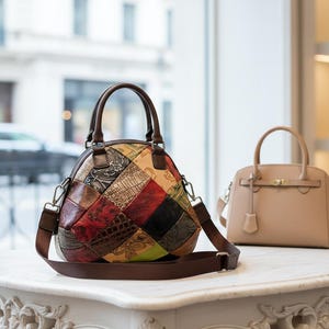 Può includere: Una borsa in pelle patchwork multicolore con tracolla e manici marroni. È visibile anche una seconda borsa color beige chiaro con manico superiore. Le borse sono esposte su una superficie bianca.