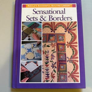May include: A hardcover book titled Rodale's Successful Quilting Library: Sensational Sets & Borders. The purple cover features a large quilt image with floral and geometric patterns, alongside three smaller inset photos showing quilting techniques.