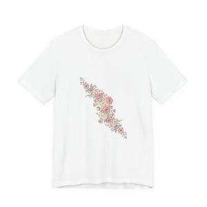 Könnte beinhalten: Weißes T-Shirt mit floralem Design. Das Design zeigt rosa und cremefarbene Rosen mit grünen Blättern und Bändern. Die Rosen sind diagonal über dem T-Shirt angeordnet.