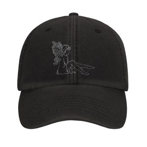 Può includere: Cappellino da baseball nero con visiera curva. Il cappellino presenta un disegno ricamato bianco di una fata seduta con ali dettagliate. Classica costruzione a sei pannelli, bottone superiore e cinturino regolabile.