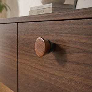 May include: Close-up of a wooden cabinet with a dark brown finish. The cabinet features a rounded, oval-shaped wooden knob with a dark metal base. The wood grain is visible on the knob and cabinet surface. The word "KINFOLK" is visible on a book.
