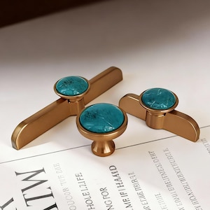 May include: A set of four bronze-colored cabinet hardware pieces. Each piece features a round, turquoise stone set in a bronze base. The hardware includes two handles and two knobs, suitable for drawers or cabinets.