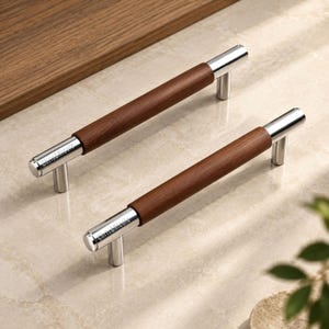 May include: Two cylindrical cabinet pulls featuring a central dark brown wood grain section flanked by polished chrome metal ends. Each chrome end is engraved with the text Chris&Nicole. The hardware includes two vertical mounting posts.