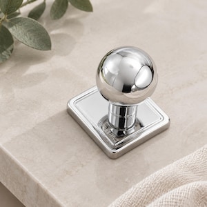 May include: A polished chrome cabinet knob featuring a spherical head attached to a square base plate. The base plate is engraved with the text "CHRIS & NOLE" in a clean, sans-serif font. The hardware has a reflective, mirror-like metallic finish.