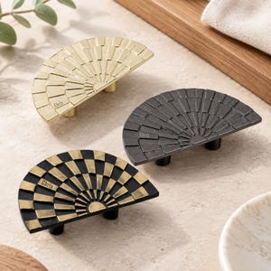 May include: Three semi-circular cabinet pulls with a fan-like pattern. One is gold, one is matte black, and one is a combination of black and gold. Each pull features the name Chris engraved on the surface and includes two mounting posts.