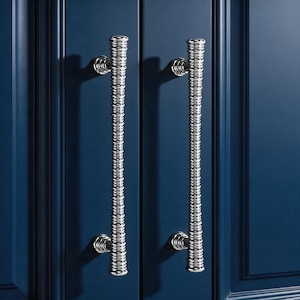 May include: Two vertical cabinet pulls with a polished chrome finish and a textured, ribbed cylindrical design. Each handle is mounted with two circular bases, featuring a repeating horizontal grooved pattern along the length of the metal bar.