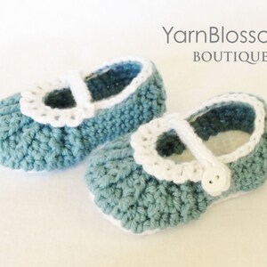 May include: A pair of crocheted baby shoes in a light blue color with white crocheted trim and a white button. The shoes have a simple, classic design.