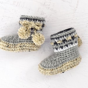 Pode incluir: Um par de sapatinhos de beb&eacute; em crochet cinzento e bege com pompons.
