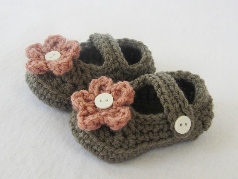 May include: A pair of brown crocheted baby shoes with pink flower embellishments and white buttons.