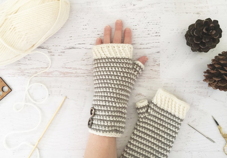 May include: A pair of fingerless gloves with a striped pattern in beige and white. The gloves have a button detail on the wrist.