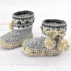 Pode incluir: Um par de sapatinhos de beb&eacute; em crochet cinzento e branco com pompons bege.