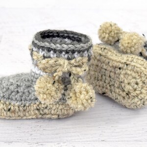 Pode incluir: Um par de sapatinhos de beb&eacute; em crochet cinzento e bege com pompons.
