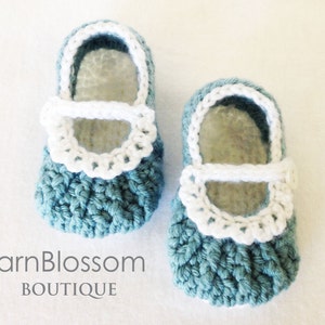 May include: A pair of crocheted baby shoes in teal blue with white trim and a white strap. The shoes have a scalloped edge around the top.