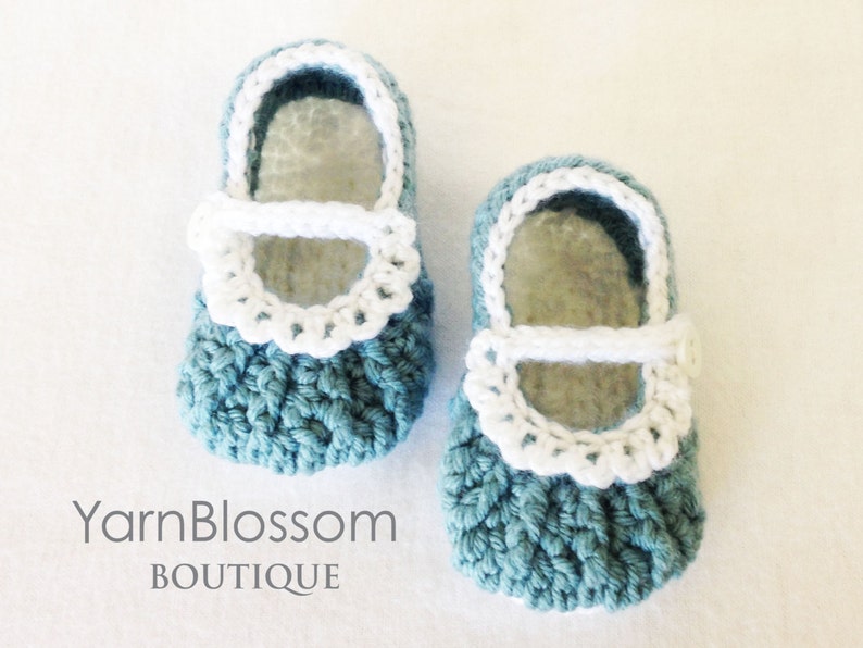 May include: A pair of crocheted baby shoes in teal blue with white trim and a white strap. The shoes have a scalloped edge around the top.