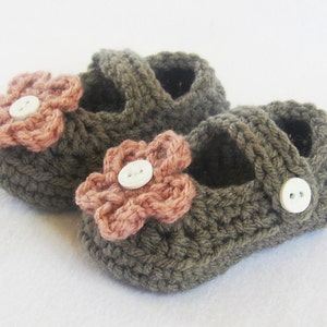 May include: A pair of brown crocheted baby shoes with pink flower embellishments and white buttons.