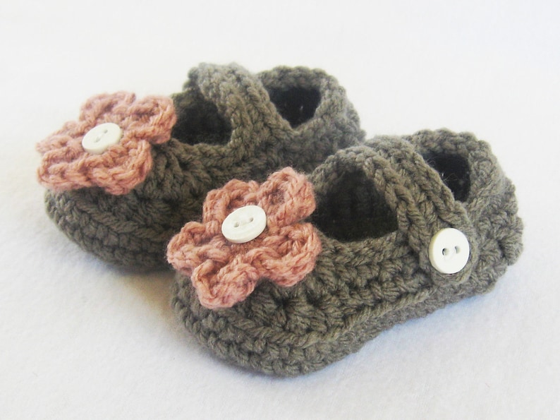 May include: A pair of brown crocheted baby shoes with pink flower embellishments and white buttons.
